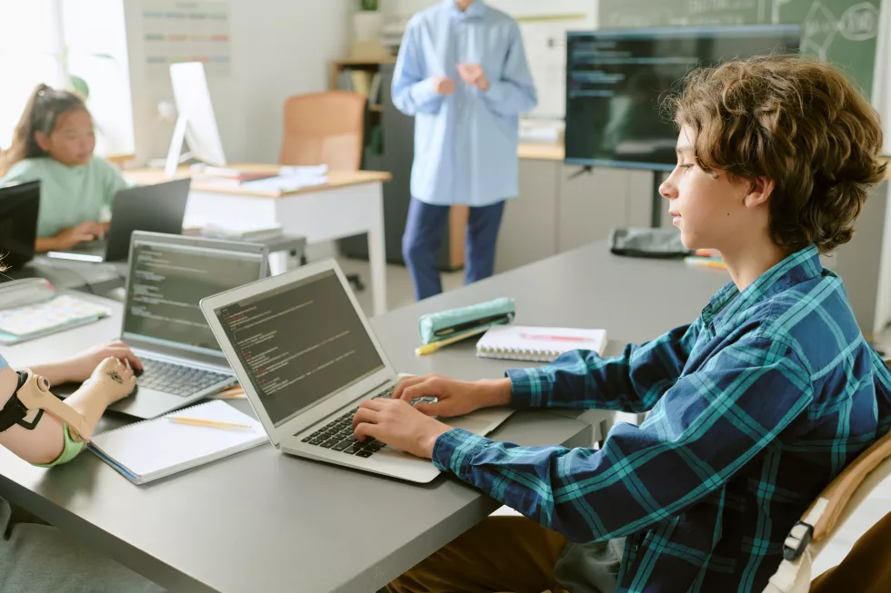 teenage-caucasian-boy-coding-laptop-classroom-with-diverse-students