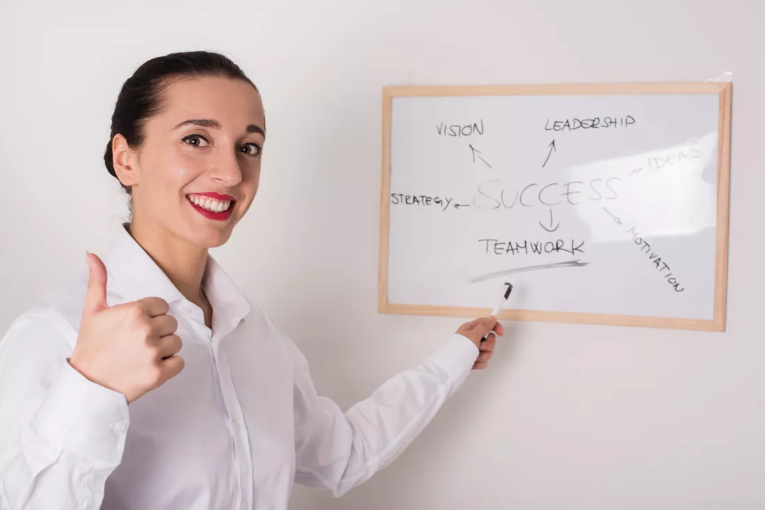portrait-smiling-businesswoman-gesturing-thumb-up-while-pointing-whiteboard-office