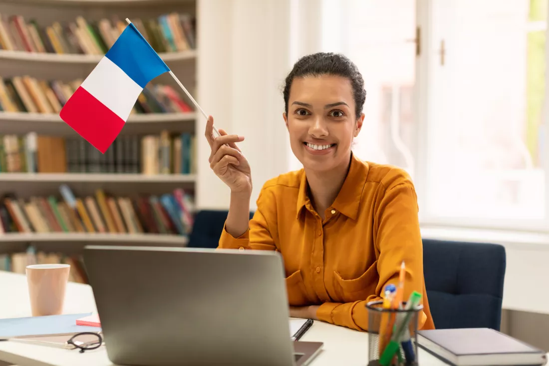 cheerful-mixed-race-female-teacher-giving-french-class-communicating-laptop-sitting-library-interior